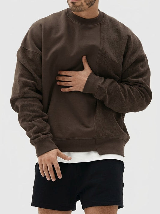 A man wearing a dark brown crewneck sweatshirt and black shorts, shown from the chin down against a light gray background.