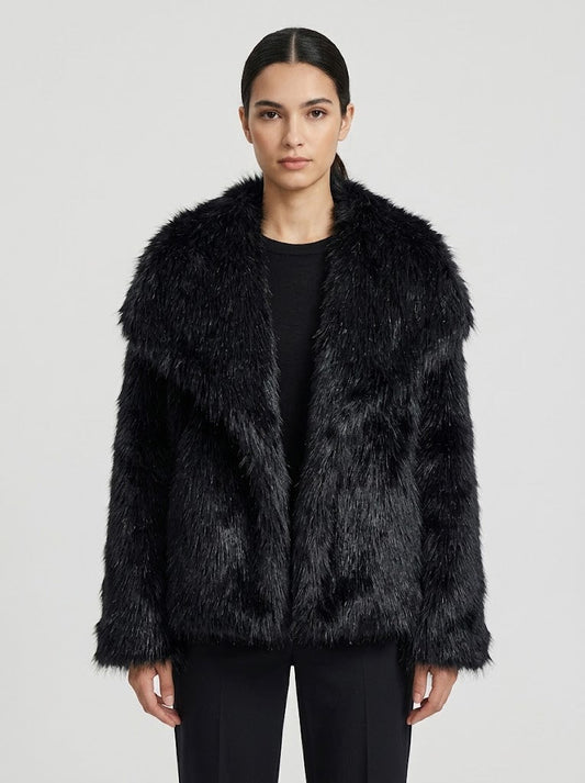 A model wearing a black faux fur jacket with a wide collar over a black top and black pants, photographed against a light gray studio background.