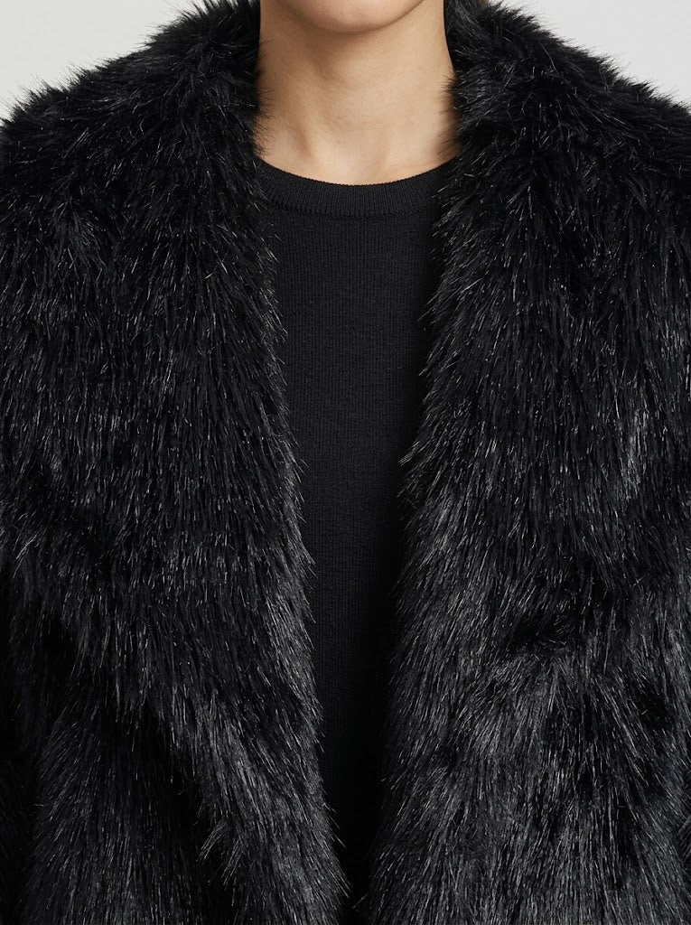 Close-up of a person wearing a black shaggy faux fur jacket over a black crewneck top, showing the texture of the fur against a light gray background.